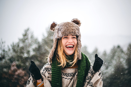 Beautiful young plus size woman listening to music via headphones in a snowy park in winter.