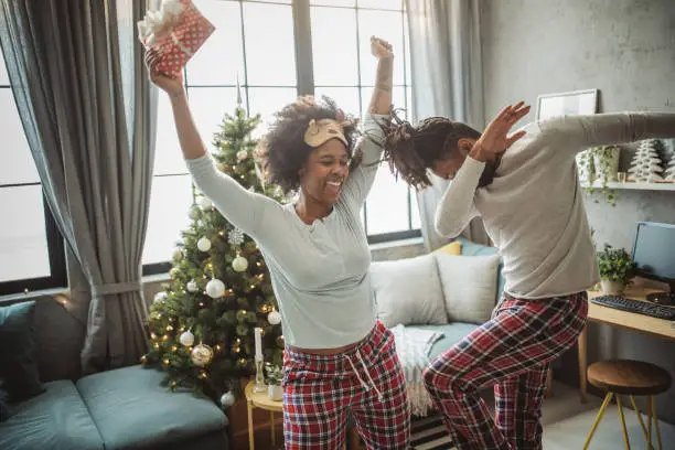 Young couple celebrating Christmas at home. Home is decorated with Christmas ornaments and lights, they exchanging presents and dancing out of happiness