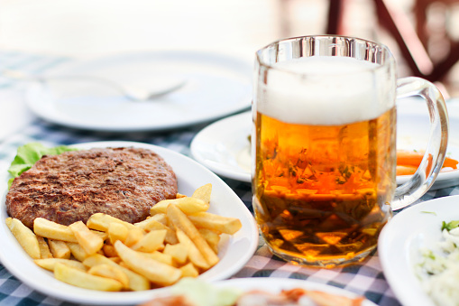 Meal - burger and fries on a plate and beer in a glass mug served on the table.