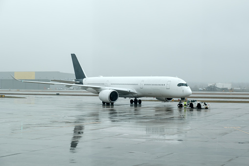 Close white narrow-body passenger airplane taxing on runway for take off on a rainy day