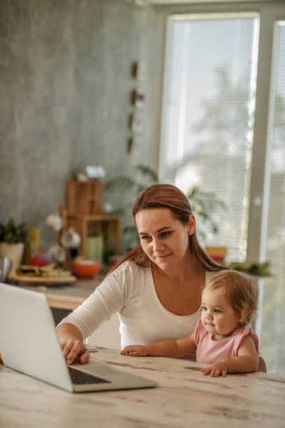 istock Woman cuddling her baby daughter while using laptop 1183657079