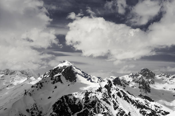 istock Black and white view on snowy sunlit mountains in clouds 1183657329