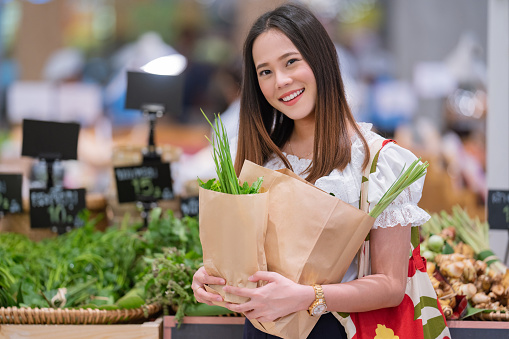 Asian woman buy vegetables in the supermarket. She uses paper bags and woven bags. For the environment