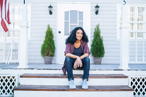 Smiling mid adult woman sitting on stairs in front of her house