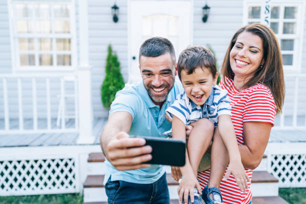 istock Parents with child having fun in front yard and taking selfie 1183697757