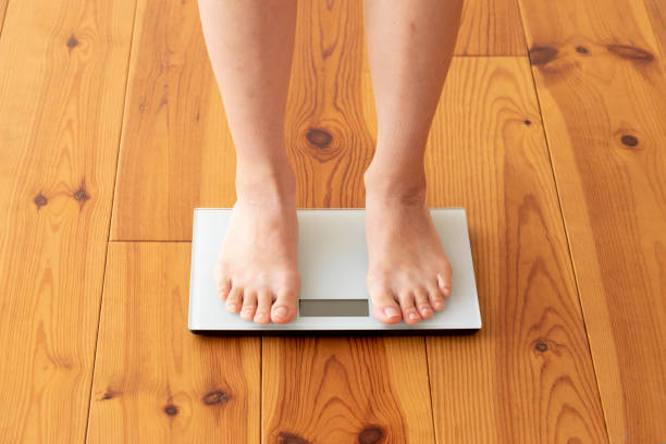 istock Young woman's feet on wooden floor and weight scale 1183701708