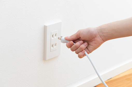 Hand of young woman plugging cord into outlet
