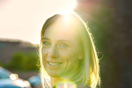 Attractive blond woman backlit by sun flare over her forehead smiling at the camera in a close up head portrait