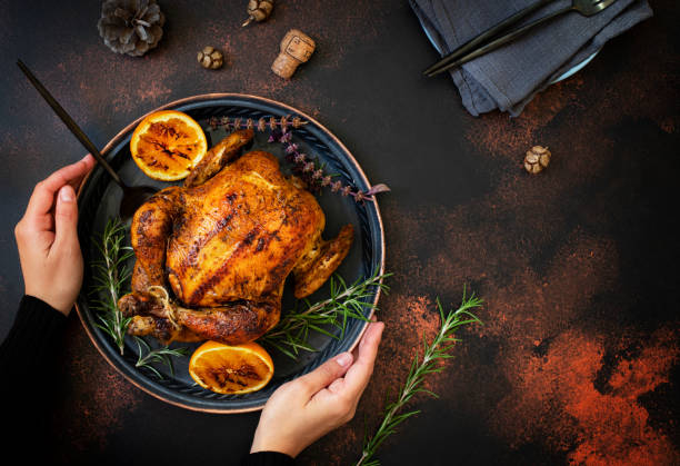 Baked whole chicken with oranges and rosemary. Female hands holding a tray with a festive Christmas dish on a dark rustic background. Top view, flat lay. Copyspace Baked whole chicken with oranges and rosemary. Female hands holding a tray with a festive Christmas dish on a dark rustic background. Top view, flat lay. Copyspace turkey thanksgiving dinner cooked stock pictures, royalty-free photos & images