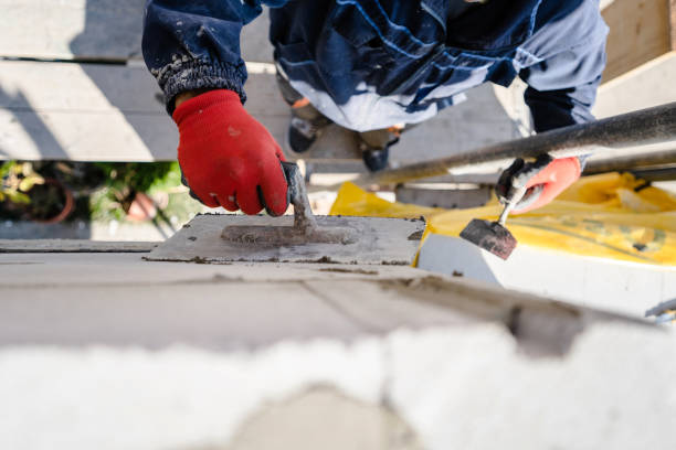 istock Construction worker plastering a wall with trowel cement mortar applying adhesive cement on the Autoclaved aerated concrete AAC brick high angle close up on hand holding the tool outdoor 1183707979
