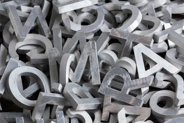 pile of silver metal alphabet characters cutted by waterjet machine - close-up view with selective focus