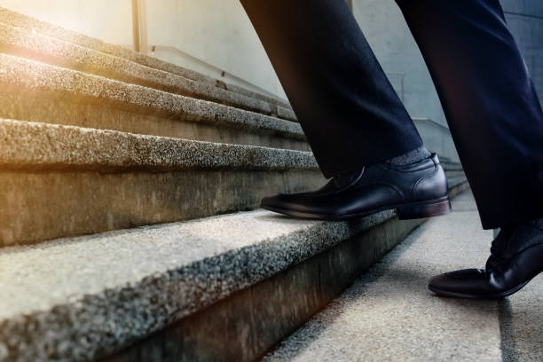 istock Motivation and challenging Career Concept. Steps Forward into a Success. Low Section of Businessman Walking Up on Staircase. Male in Black Formal Dress 1183711171