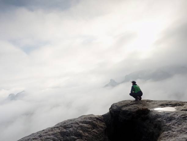 istock Man sitting on cliff enjoying mountains and clouds landscape 1183711290