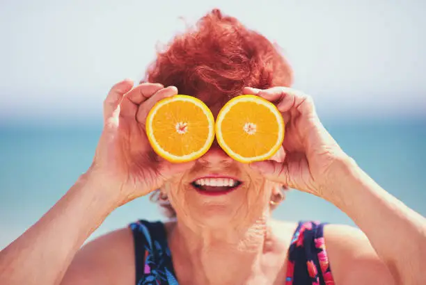 Photo of funny portrait of happy mature woman, grandma having fun with orange eyes on summer vacation. Active lifestyle