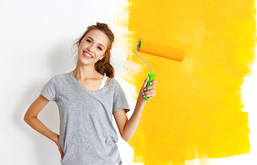 Repair in the apartment. Happy young woman paints the wall with  yellow  paint