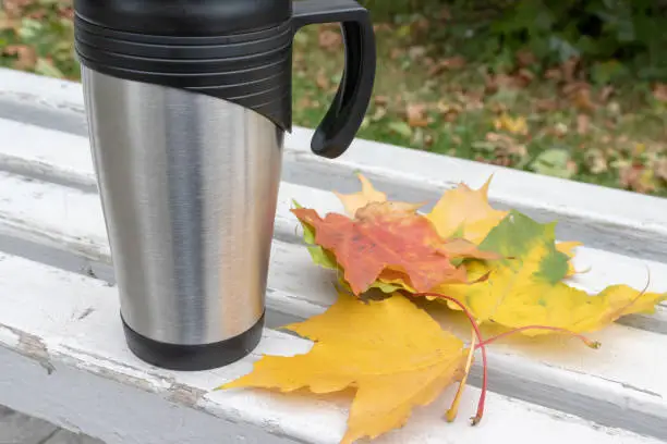Season, autumn hot drinks and picnic concept - metal thermo coffee cup surrounded by colorful yellow leaves.