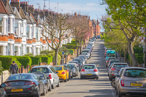 London, UK - 10 April, 2019 - A car driving through a London street lined with terraced houses and parked cars around Crouch End area