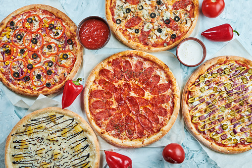 Many kinds of tasty pizza with salami, meat and chicken on light background. Table with many italian homemade pizza. Flat lay food