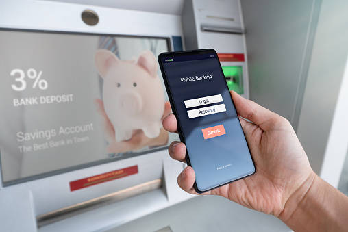 Withdraw money from an ATM without using a credit card. Person holding a phone with a login screen for mobile banking.