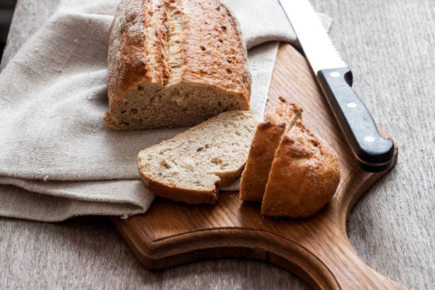 istock Loaf of whole wheat bread with slices on wooden board on kitchen table 1183733155