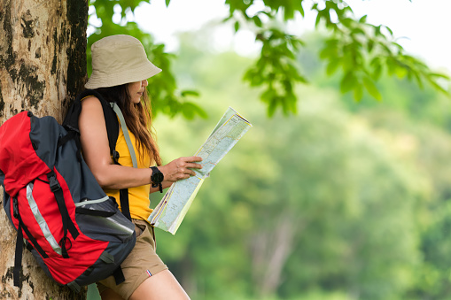 Asian women and traveler and tourism with backpack adventure holding map to find location directions and leisure destination place in the jungle forest outdoor nature. Travel Concept