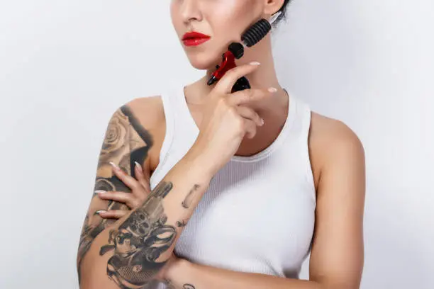 Young woman tattooist with a tattoo-machine in her hand on white background
