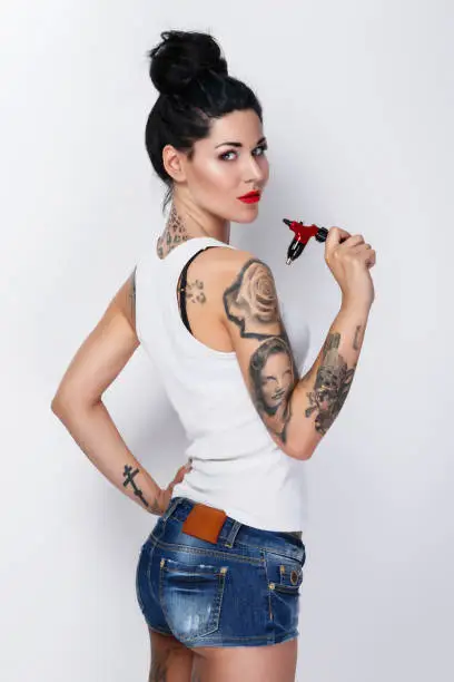 Young woman tattooist with a tattoo-machine in her hand on white background