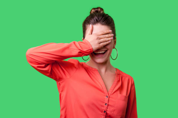 Don't want to watch! Portrait of positive elegant woman with bun hairstyle, big earrings and in red blouse. indoor studio shot isolated on green background Don't want to watch! Portrait of positive elegant woman with bun hairstyle, big earrings and in red blouse standing covering eyes with hand and smiling. indoor studio shot isolated on green background red blindfold stock pictures, royalty-free photos & images