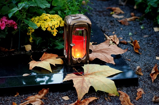 Grave light in evening mood on a cemetery with autumn leaves