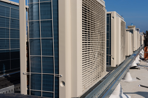 Air conditioner units (HVAC) on a roof of new industrial building with blue sky and clouds in the background.