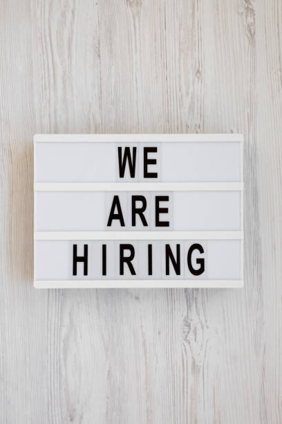 istock 'We are hiring' words on a lightbox on a white wooden surface, overhead view. Top view, from above, flat lay. 1183748358