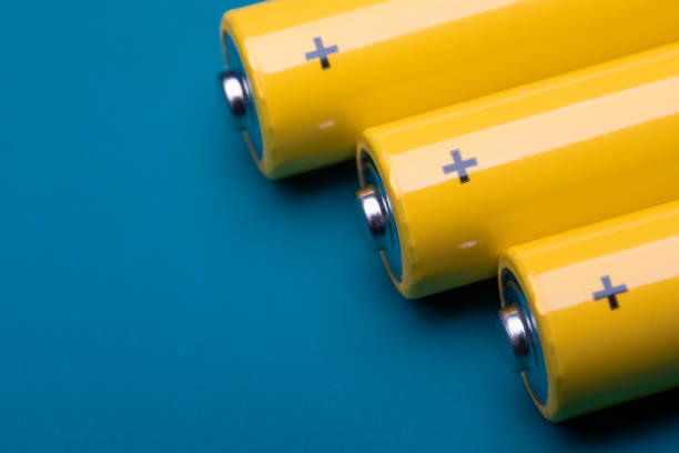 Yellow alkaline batteries on blue background Close up shot of yellow AA alkaline or rechargeable NiMH batteries on blue background, shallow focus e waste photos stock pictures, royalty-free photos & images