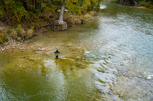 A teen fly-fisherman casting on a trout stream.  Shot from a high angle with lots of copy space.