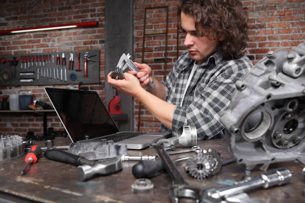 istock man work with caliper measure the motor gear, study on the computer and search in internet spare engine parts on the workbench in home garage workshop, diy concept 1183754796