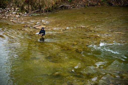 A young fly fisherman casting to a Chinook salmon in the tail of a pool on a Great Lakes tributary river.  The salmon is visible in the center bottom of the frame in front of the rock.