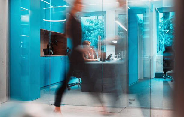 Defocused background of an office space, with beige floor and white furniture, blue glass partitions, desk and chairs. Bright, with sunlight. No people. Blurred background with copy space. Blue and beige hues.