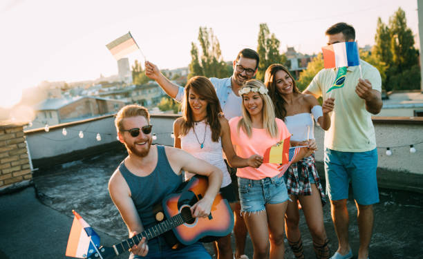 istock Young friends having fun at a rooftop party, playing the guitar, singing, dancing and drinking 1183760717
