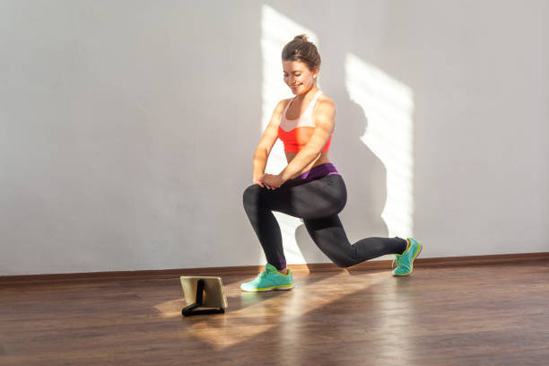 fleißig eispositiv fit frau mit brötchen frisur und in engen sportbekleidung tun kniebeugen. indoor-studio-aufnahme beleuchtet durch sonnenlicht aus dem fenster - the splits ethnic women exercising stock-fotos und bilder