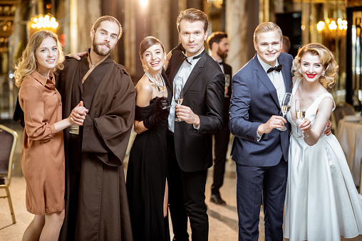 Portrait of an elegant group of people dressed in retro style standing together with wine during the grand celebration at the luxury restaurant hall