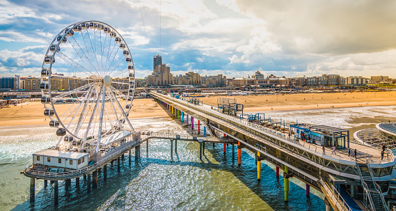 Colorful image with the ferris wheel and pier at the beach of Scheveningen at The Hague. Skyline in the background. Cloudy day with sunshine on a late summer day. Popular attraction and landmark for tourists.