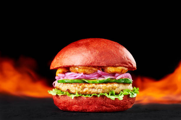 istock Red Burger in fire flames at dark background. Burger with red bun, chicken cutlette, onion, prawns and avocado. Copy space 1183764926