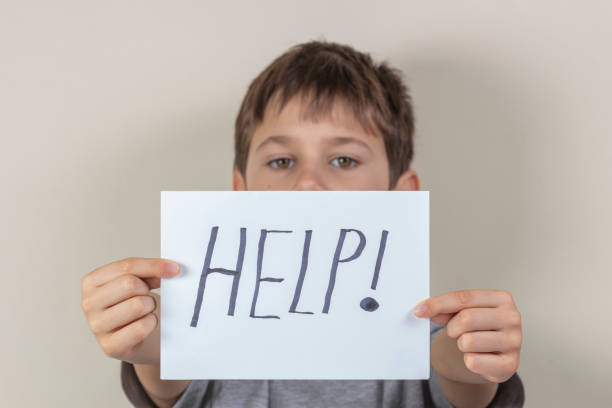 istock Help sign. Unhappy child holding paper with word Help 1183766216