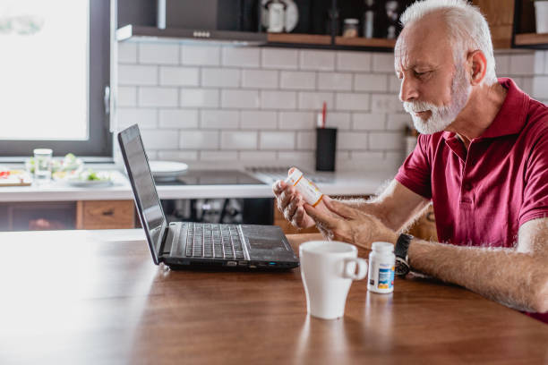 Searching online about medicine Senior man is looking for information about the medicine over the Internet. He is holding a medicine in one hand prescription medicine photos stock pictures, royalty-free photos & images