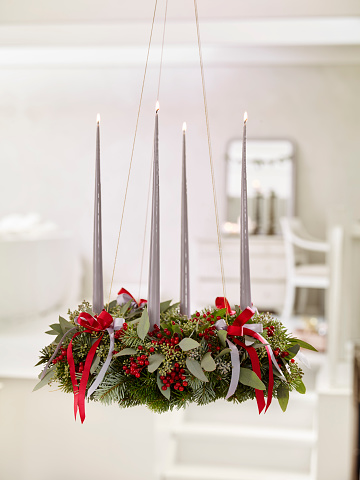 Hanging advent wreath with lit candles and ribbons and red berries