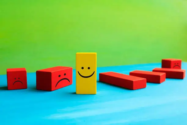 Photo of Happy and sad face emojis on wood blocks toys and green background.