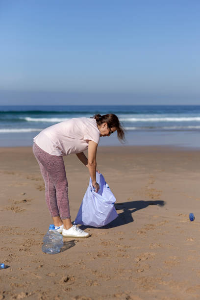istock Woman picking up trash and plastics cleaning the beach 1183778864