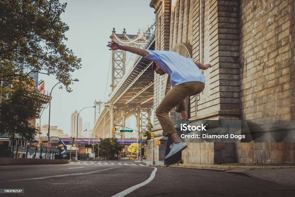 Skater training in a skate park in New York Young adult skating outdoors - Stylish skater boy training in a nNew York skate park, concepts about sport and ifestyle Brooklyn Bridge Stock Photo