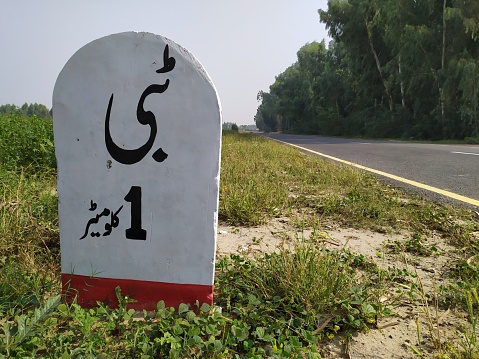 A beautiful white coloured milestone beside the road leading to a beautiful village.