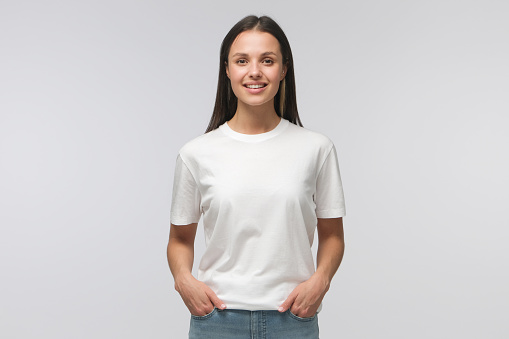 Young female standing in front of camera in white T-shirt and blue jeans, isolated on background