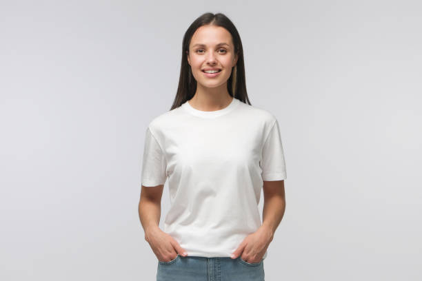 Young female standing in front of camera in white T-shirt and blue jeans, isolated on background Young female standing in front of camera in white T-shirt and blue jeans, isolated on background white people stock pictures, royalty-free photos & images